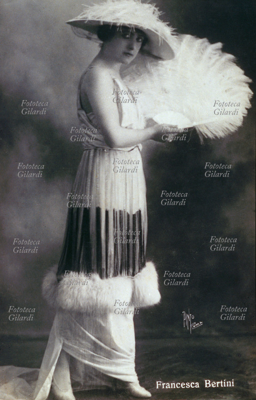 Francesca Bertini (1892) actress. Portrait to entire figure with unglued dress, fan and hat with piume of ostrich. Its reputation of beautiful and fatal woman gave origin to the divismo in Italy. Taken part to beyond 90 films, some: Assumed Thorn (1915), Fedora (1916), nude woman (1918).