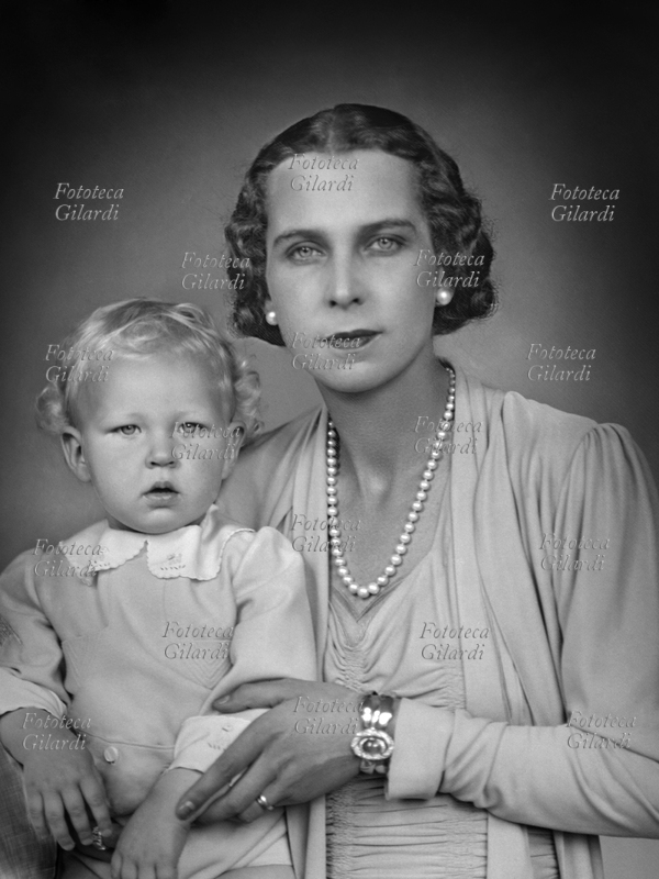 MARIA JOSÉ del Belgio (4 agosto 1906 – 27 gennaio 2001) Marie José Carlotta Sophia Amelia Enrichetta Gabriella di Sassonia Coburgo-Gotha, Principessa consorte del Piemonte in quanto moglie del futuro Umberto II dal 1930, con il secondogenito Vittorio Emanuele (12 febbraio 1937 – 3 febbraio 2024). La principessa è aiutata dalla balia nel sorreggere il piccolo, ma non si vede grazie al ritocco e al taglio dell\