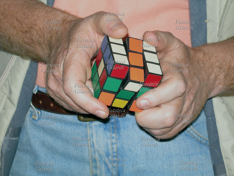 GIOCHI dettaglio delle mani con il Cubo di Rubik di un giocatore adulto in cerca della soluzione. Il gioco rompicapo fu inventato dal professore di architettura e scultore ungherese Ernö Rubik nel 1974. Lo scopo del gioco è di risalire alla posizione originale dei 26 cubetti portando il cubo ad avere per ogni faccia un colore uguale. Il cubo può assumere ben 43.252.003.274.489.856.000 combinazioni diverse, solo una delle quali è quella corretta. Il gioco divenne molto diffuso e popolare, la stima delle vendite nel 1982 superava i 100 milioni di pezzi.