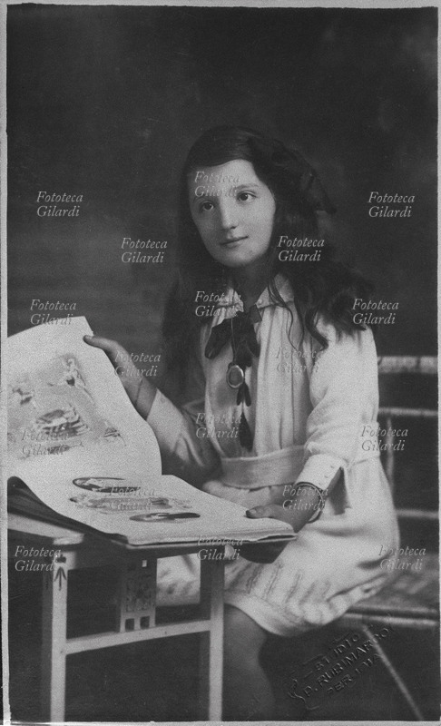BAMBINA in posa per una fotografia ricordo mentre sfoglia un album. Perugia, 1915 circa.