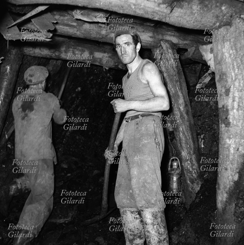 MINIERA due minatori al lavoro nella antichissima miniera di lignite a Luni, detta la Lunara, da cui si estraeva già dal tempo degli Etruschi. La lignite è un carbone fossile con caratteristiche di combustibile poco pregiate, entrato in disuso nel secondo dopoguerra (1950-60). Gli operai occuparono questa miniera nel tentativo di impedirne la chiusura, che poi invece avvenne con conseguente licenziamento dei lavoratori. Fotografia di Ando Gilardi (1921-2012) #andogilardi, eseguita con illuminazione di bulbi al magnesio. Luni (La Spezia), 1953.