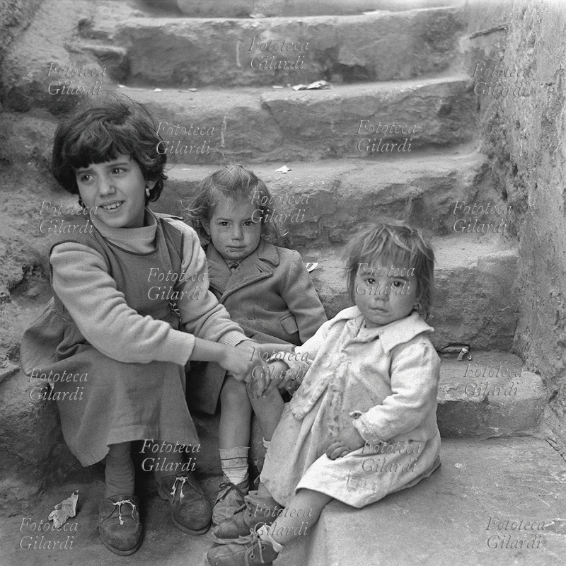 BAMBINI tre bambine giocano sulla scala di casa: la più grande tiene la mano alla più piccola. Colpisce la povertà dell\