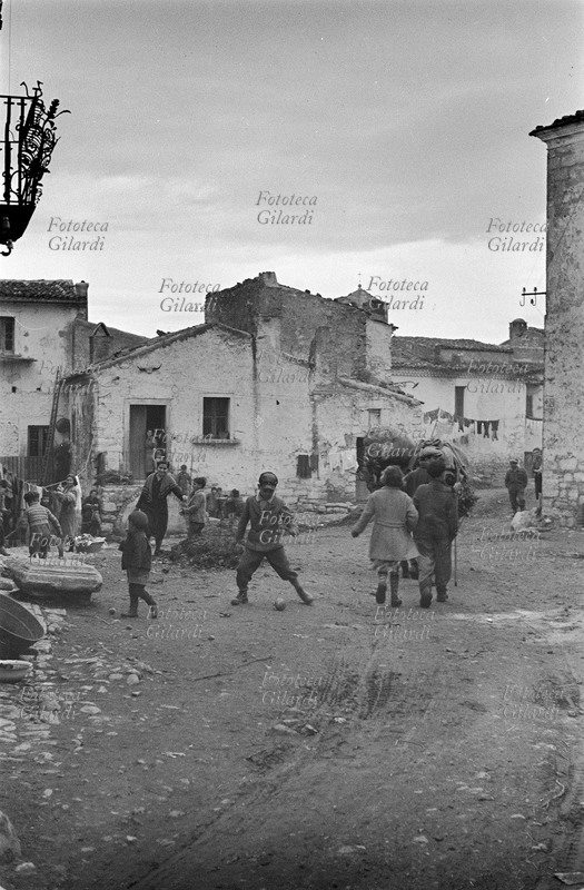 ITALIA Venosa, giochi di bambini tra le abitazioni in via Roma; si notano i mucchi di fango ammassati dai manifestanti durante lo sciopero a rovescio, che avrebbe dovuto sensibilizzare le autorità verso un utilizzo dei disoccupati nella manutenzione delle strade, col duplice beneficio di creare lavoro e migliorare le condizioni di vita. Fotografia di Ando Gilardi (1921-2012) #andogilardi, parte di un ampio servizio realizzato per \