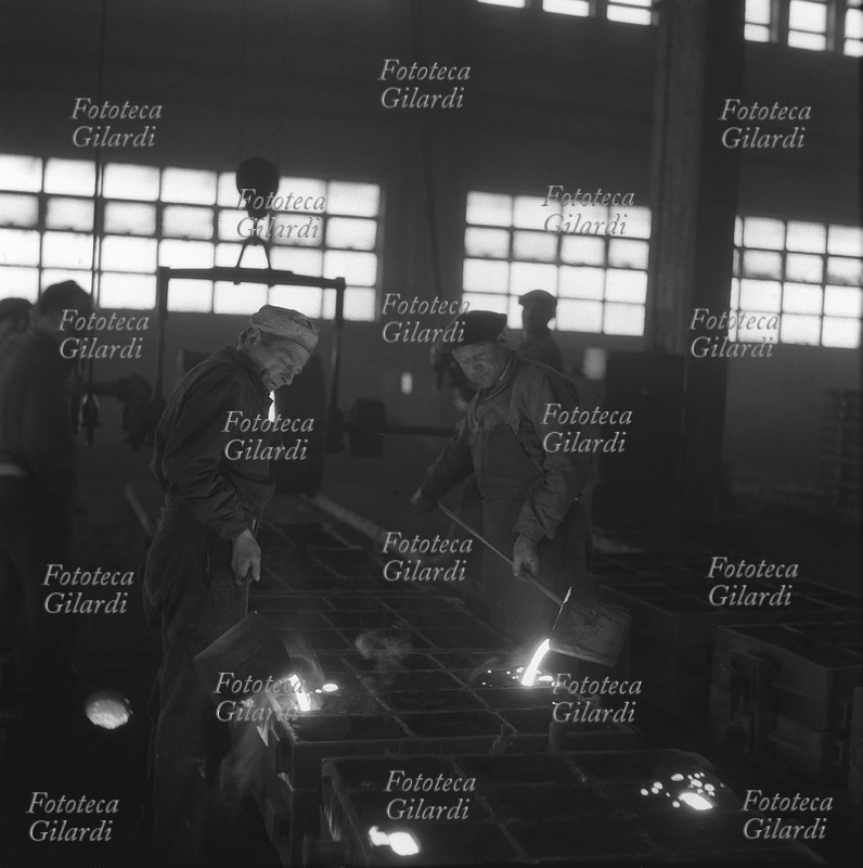 MESTIERI Due operai in officina colano il metallo incandescente in una serie di stampi, suggestiva e drammatica atmosfera infuocata. Firenze, lotta alla Pignone. Il lavoro continua nella fabbrica occupata dalle maestranze per 80 giorni, da luglio a settembre 1953. Fotografia di Ando Gilardi (1921-2012) #andogilardi, Italia 1953.