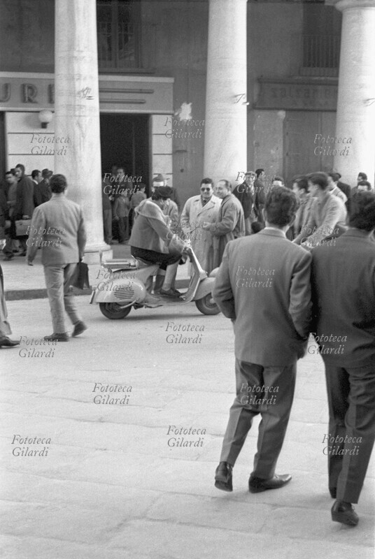 CARNEVALE un uomo, mascherato da donna, gira in scooter per le strade della cittadina: tutti si girano a guardare divertiti dalla scena. Fotografia di Ando Gilardi (1921-2012) #andogilardi, Crotone 1957.