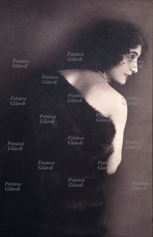 Anna FOUGEZ (Anna Pappacena, 1898-1966) ritratta di spalle, avvolta in una pelliccia scura, con una spalla nuda. Attrice italiana di varietà, raggiunse grande popolarità tra gli anni Venti e Trenta sui palcoscenici italiani e francesi. Fra l\