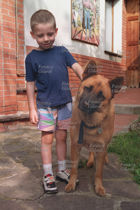 BAMBINI Bambino e cane, grandi amici e compagni di giochi. Ritratto di Francesco con il cane femmina Luna. Lui la guarda sorridendo e accenna una carezza, lei guarda curiosa la macchina fotografica. Fotografia di Elena Piccini, Caldasio (AL) Agosto 2002.