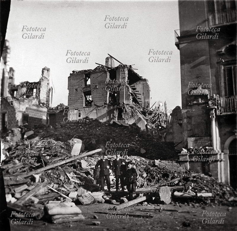 TERREMOTO CALABRO SICULO 1908 Una piazza, veduta fotografica con rovine. Al centro posano tra i resti dei palazzi tre eleganti signori. Messina, 28 dicembre 1908