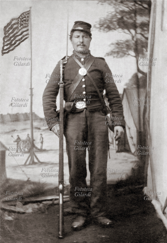 GUERRA DI SECESSIONE Fotografia ricordo di soldato federale (stati del Nord), ritratto realizzato in studio. Il fondale simula un accampamento militare con la bandiera a stelle e striscie innalzata 1861-1865