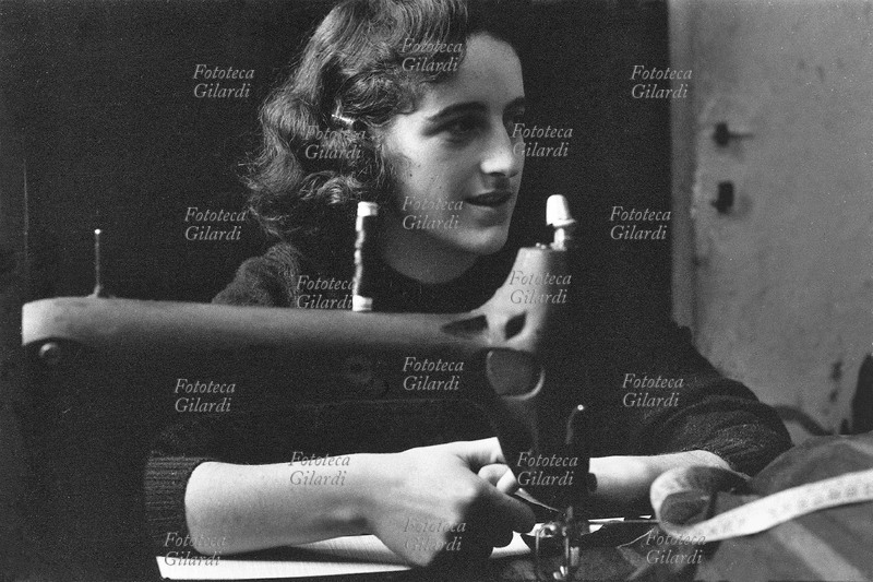 MESTIERI sarta al lavoro dietro alla macchina da cucire; la giovane sorride serenamente, ripresa di tre quarti, cuce con una delle prime \