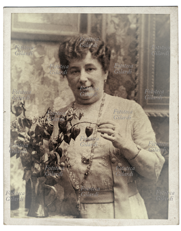 Emma ORCZY (23 September 1865 - 12 November 1947) British writer of Hungarian origin, known mainly for having conceived the popular literary saga "The red primrose" in 12 titles (the last unpublished) published since 1905. Set in France of Terror, the saga tells the adventures of the mysterious character who, ardent defender of the nobility persecuted by the revolutionaries, strives to save as many as he can from the guillotine; the counter-revolutionary monarchist hero hides behind the unsuspecting remains of the English meek Sir Percy Blakeney. Noble by birth, family events tore Emma from the comfortable country estate where she was born to take her through Budapest and Paris to London, where she arrived fifteen and finally felt at home again. From the marriage of love with the painter Montague Barstow was born John Montague Orczy-Barstow, also later writer with the pseudonym of John Blakeney, in clear tribute to the protagonist of the maternal successes. Lover of travels, Emma shared the residences of Monte Carlo and Lerici with her husband as well as the London residence. Photographic portrait in the studio in front of a jar of alchechengi, circa 1915