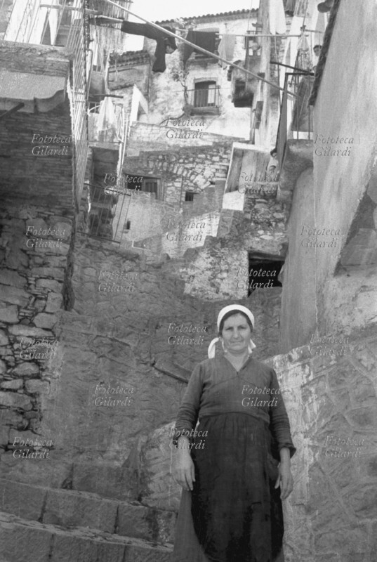BASILICATA Donna ritratta sullo sfondo del paese di Castelmezzano (PZ), arroccato sule Dolomiti lucane. Immagine presa durante la spedizione condotta in Lucania dal 15 maggio al 4 giugno 1957 con l\