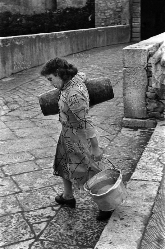 ITALIA Venosa, ragazza (la figlia di Menica) trasporta acqua, sul ponticello che conduce alla rocca dove hanno sede il PCI e la Camera del Lavoro. Nel castello vi erano anche delle abitazioni. Fotografia di Ando Gilardi (1921-2012) #andogilardi, parte di un ampio servizio realizzato per \