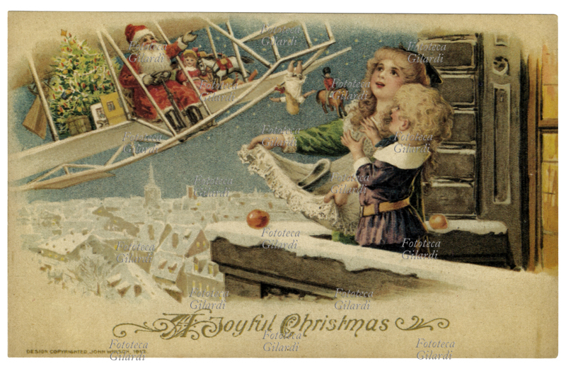 NATALE Babbo Natale moderno lancia i doni da un curioso velivolo, anzichè dalla solita slitta; due bambini raccolgono i giochi salutando dal balcone. Cartolina augurale natalizia, U.S.A. 1913