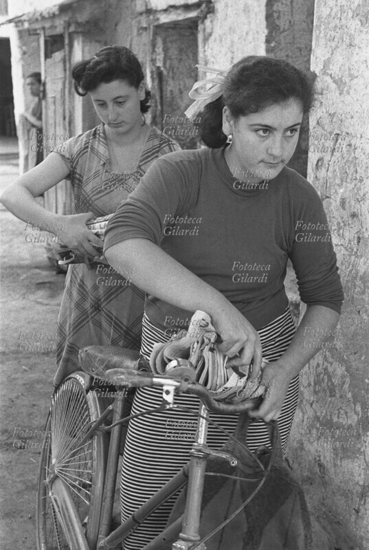 PROFESSIONS The town postwoman, with an assistant, unloads the bag with the mail to be distributed from her bicycle. Photograph by Ando Gilardi (1921 -2012) #andogilardi from \