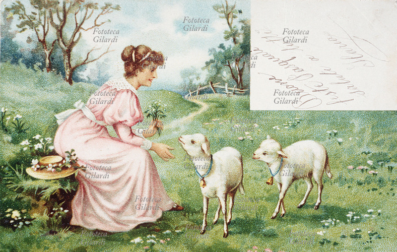 PASQUA cartolina augurale, giovane donna seduta in un prato fiorito, allunga la mano carezzevole verso due teneri agnellini. Italia, primi XX secolo.