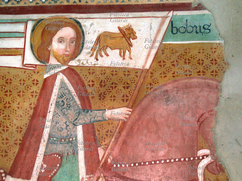 SAN BOVO (940 circa – 22 maggio 986) nobile cavaliere provenzale dedito alla penitenza e ai pellegrinaggi rappresentato a cavallo con lo stendardo che raffigura i buoi, simbolo dello spirito di sacrificio, della virtù del lavoro e della sottomissione alla Parola di Dio (particolare del Santo). Dettaglio dagli affreschi attribuiti alla scuola di Manfredino e Franceschino Boxilio sulla colonna centrale nell\