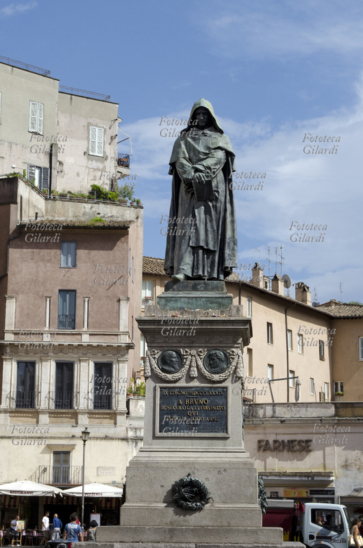 Giordano BRUNO (1548-1600) incappucciato nel saio domenicano, con le mani incrociate sul libro proibito, il volto intensamente meditativo significativamente rivolto verso la basilica di San Pietro in Vaticano. Monumento in bronzo realizzato da Ettore Ferrari (1845-1929) ed eretto il 9 giugno 1889 in Campo de\