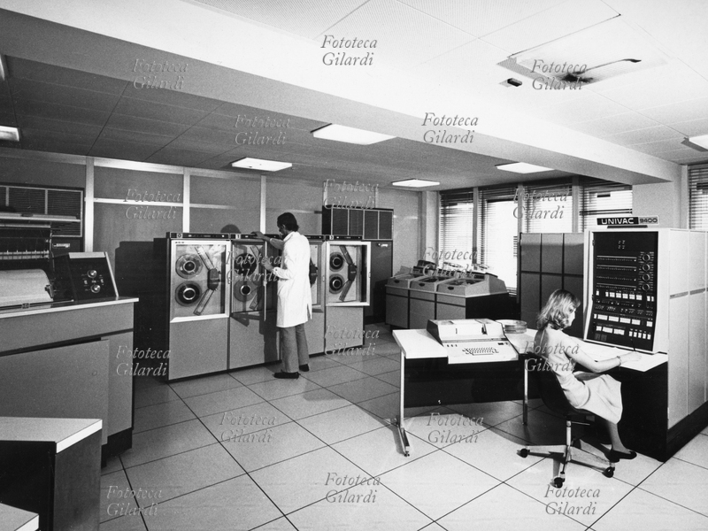 SETTORE TERZIARIO Sala di custodia delle memorie magnetiche della Banca Alto Milanese, una operatrice è alla tastiera del terminale UNIVAC 9400 e un tecnico è alle bobine delle memorie magnetiche. Busto Arsizio, fotografia di Ando Gilardi, 1970 circa