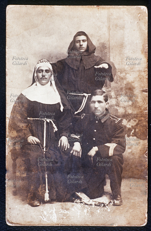TRAVESTIMENTO scherzoso di tre amici militari due dei quali si sono fatti fotografare in abiti da monaco e da suora. Fotografia virata seppia, 1910 circa