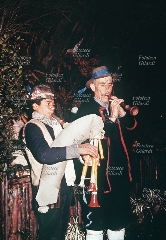 MUSICA POPOLARE Roma: Natale a piazza Navona, due suonatori ambulanti di zampogna e ciaramella intonano le tradizionali novene natalizie durante la rappresentazione del Presepe vivente. I due indossano le povere vesti in pelle di pecora dei pastori. Fotografia di Ando Gilardi (1921 - 2012) #andogilardi, Italia, 1956 circa
