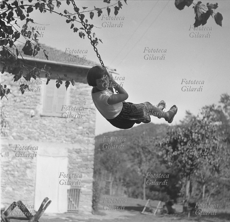 ALTALENA bambina ritratta mentre si dondola su una povera altalena: un travetto appeso ad un albero con un\
