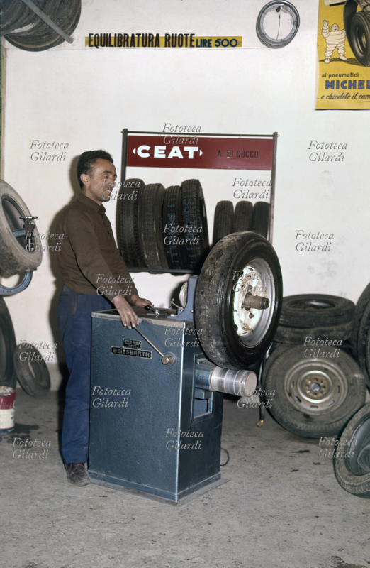 MESTIERI Operaio di autofficina addetto alla manutenzione degli pneumatici al lavoro su di una macchina utensile Beissbarth con targhetta \