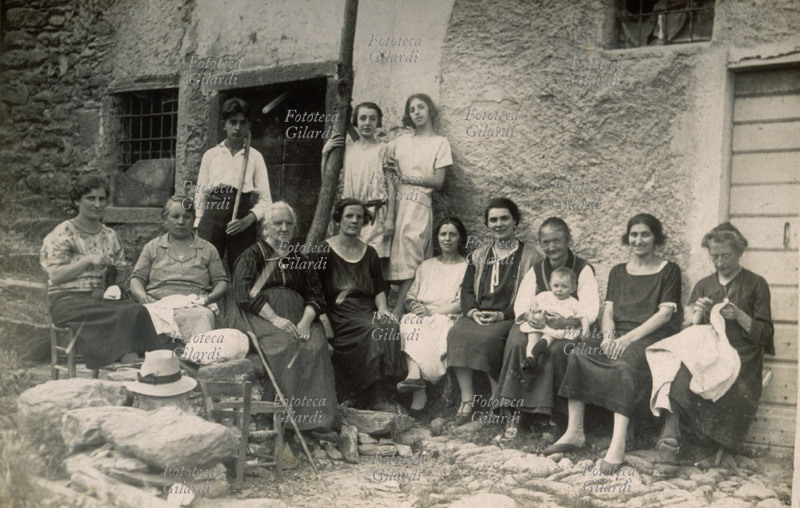 FAMIGLIA matriarcale allargata, in posa sedute nel cortile di una cascina agricola, tutte donne tranne un ragazzino in piedi dietro al gruppo insieme ad altre due adolescenti \