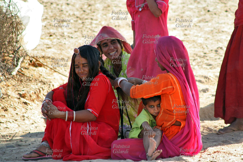 INDIA Parrucchiera del deserto che, col bimbo in grembo, pettina con lunghe trecce e acconciatura una futura sposa; nel deserto vicino a Khuri, arrivando da Jaisalmer; in fondo al deserto del Thar e vicino al Pakistan. Fotografia di Raffaella Milandri. India, Jaisalmer novembre 2007