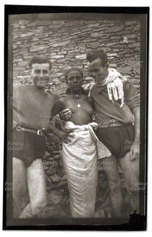 COLONIALISMO A.O.I. due soldati posano in una fotografia spontanea, assumendo un odioso atteggiamento da conquistatori carnali nei confronti di una giovane africana, 1935 - 1936