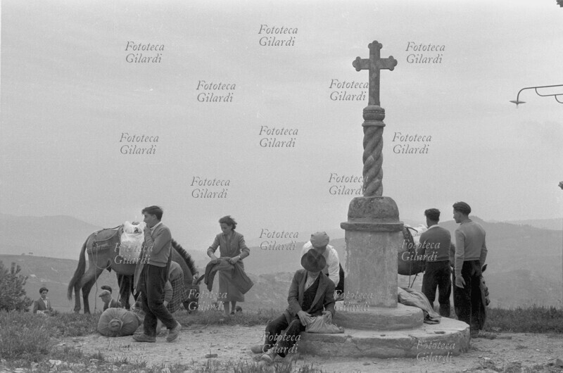 PELLEGRINI una tappa del pellegrinaggio diretto al Santuario di Santa Maria di Fonti a Tricarico (Matera): momento di riposo presso la croce. Fotografia di Ando Gilardi (1921 - 2012) #andogilardi, Italia 1957.