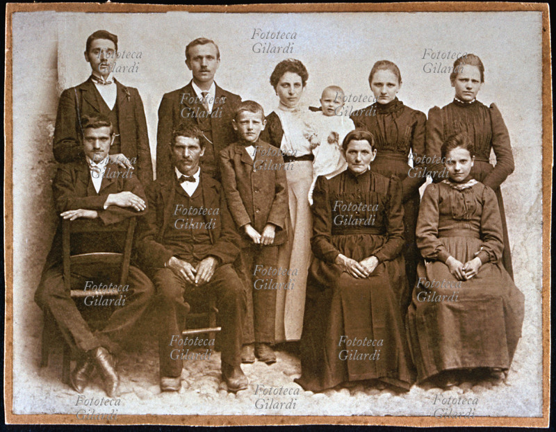 FAMIGLIA numerosa, fotogruppo composto dai genitori, seduti al centro, con gli otto figli, la più giovane tenuta in braccio dalla balia. Fotografia di anonimo, eseguita in esterno. Italia, 1895 circa.