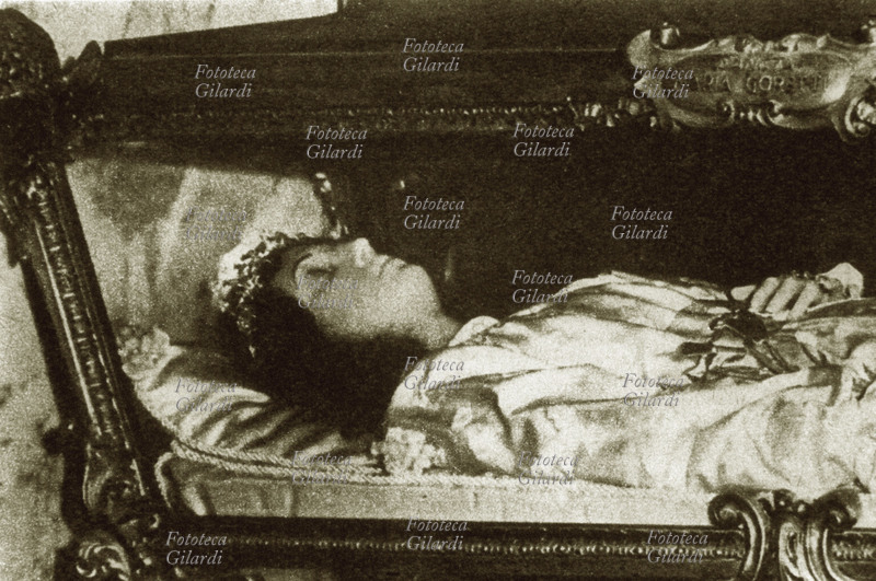 Maria GORETTI (16 ottobre 1890 – 6 luglio 1902), venerata come santa e martire dalla Chiesa cattolica; il suo corpo imbalsamato, nel sarcofago di vetro conservato nella Chiesa a lei dedicata a Nettuno RM. La giovane fu santificata per avere preservato la sua purezza al prezzo della morte. Fu infatti aggredita con 14 colpi di punteruolo, a undici anni, il 5 luglio 1902, da un giovane vicino che voleva insidiarla, ma che lei aveva risolutamente respinto; morì il giorno seguente in ospedale. Fotografia, inizio del XX secolo.