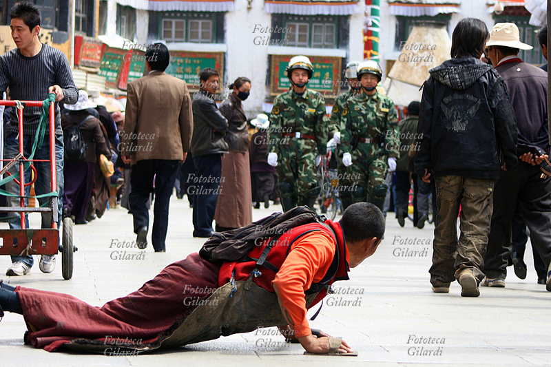 TIBET Lhasa, siamo nel Barkhor, che è la kora (percorso di preghiera) attorno al Jokhang di Lhasa. Un pellegrino buddista si prostra in preghiera mentre sopraggiungono soldati dell\
