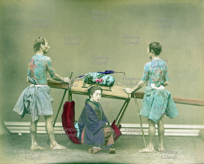 GIAPPONE 1890 Donna trasportata in portantina da due uomini dal torso tatuato, periodo Meiji (1868-1912). Fotografia colorata manualmente, 1890.