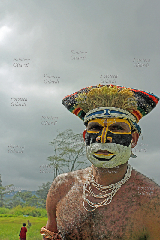 OCEANIA Uomo della tribù Kunai con il volto dipinto in giallo, nero e bianco, con numerosi giri di perline intorno al collo e perline che decorano anche il variopinto copricapo. Indossa il costume tribale per il festival di "Sing Sing", che dal 1961 riunisce ogni anno a Mount Hagen migliaia di guerrieri e partecipanti vari di tutte le tribù della regione, che celebrano e consolidano la convivenza pacifica esibendosi in competizione nelle proprie danze accompagnate da musiche e canti tribali, per due giorni, nei costumi tradizionali, con il volto e il corpo dipinti nei colori rituali. Fotografia di Raffaella Milandri, Mount Hagen, Papua Nuova Guinea, 17 agosto 2013