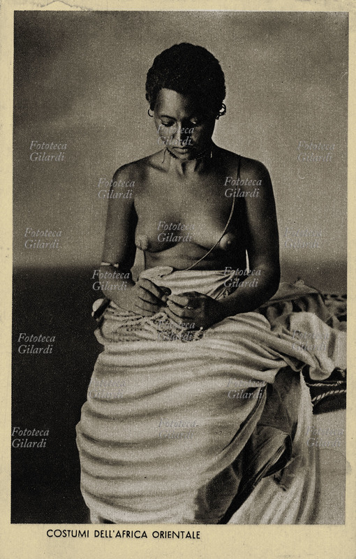 COLONIALISMO A.O.I. giovane donna africana seduta, indossa solo un pareo, portato appoggiato sulle anche. Il titolo: \