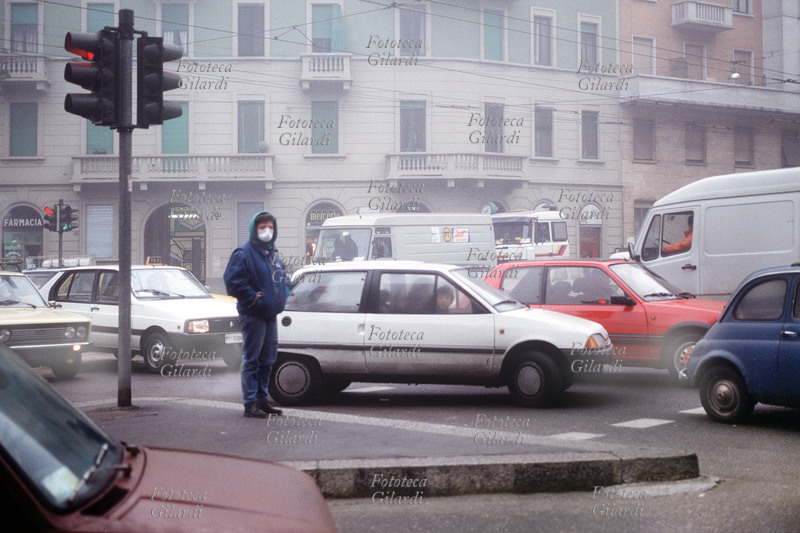 INQUINAMENTO Un pedone con la mascherina si protegge dalle polveri nocive dei gas di scarico delle automobili. Fotografia di Elena Piccini, Milano, febbraio 1989