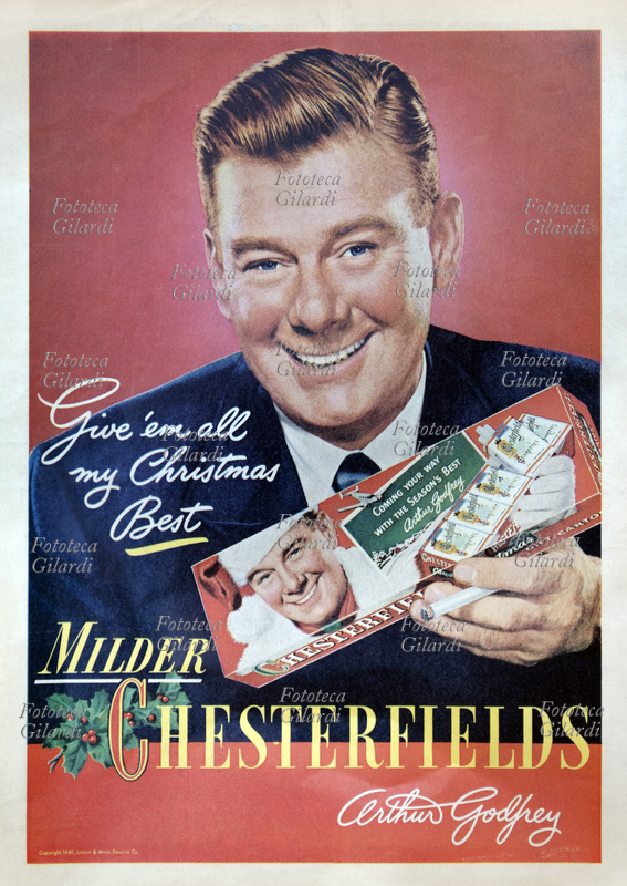 FUMO pubblicità per le sigarette Milder Chesterfields: Arthur Godfrey (31 agosto 1903 - 16 marzo 1983) offre le sigarette nella confezione natalizia, in cui figura vestito da Babbo Natale. Il popolare intrattenitore televisivo e radiofonico è stato per parecchi anni testimonial di questa marca di tabacco, per la quale ha inventato lo slogan "comprati la stecca"; ha interrotto il contratto intorno al 1954, quando ha smesso di fumare, cinque anni prima che gli venisse diagnosticato un cancro ai polmoni. In seguito è diventato un convinto sostenitore della campagna antifumo. USA, dicembre 1949.