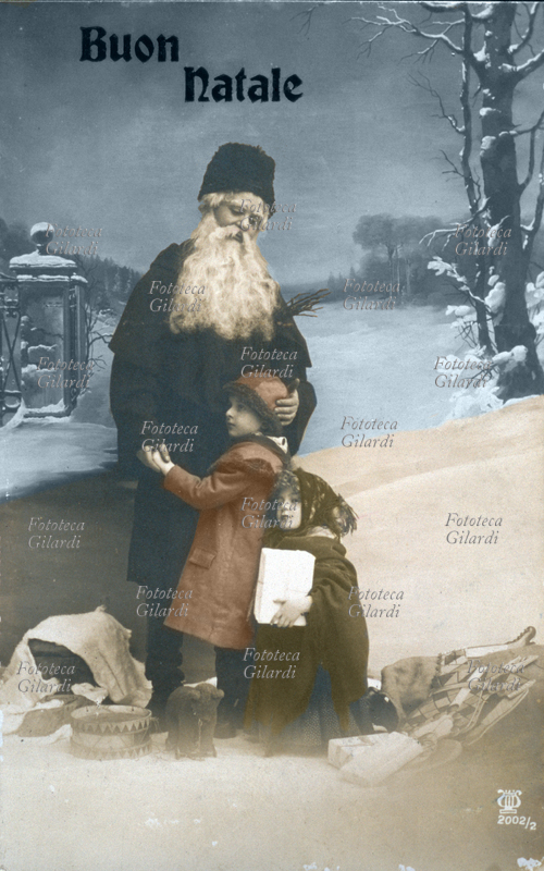 NATALE Babbo Natale porta giocattoli ad un bambino e una bambina che lo abbracciano, teneramente ricambiati. Fotografia di studio, viraggio blu e seppia, con fondale che raffigura un paesaggio innevato. Italia, 1915.