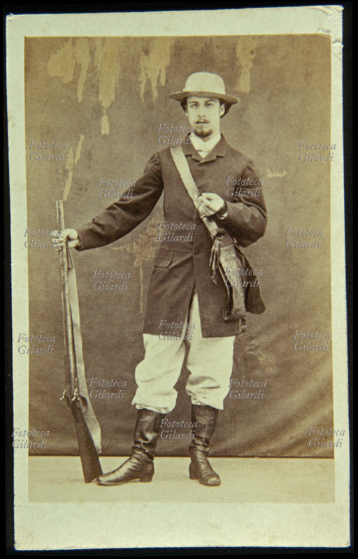 CACCIA cacciatore in posa con fucile, in completo abbigliamento da caccia. Poco rassicurante è lo sguardo, che presenta un evidente strabismo, in considerazione del fatto che l\