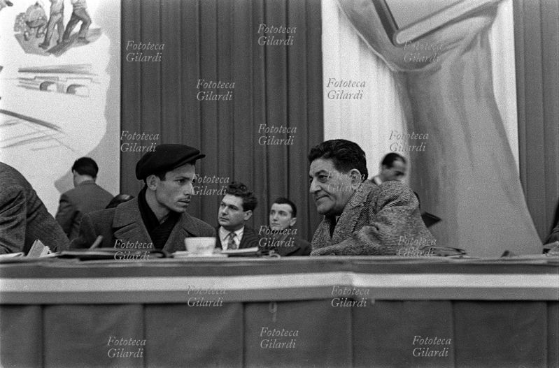 Giuseppe DI VITTORIO (1892-1957) sul palco discorre con il figlio di Paolo Vitale, bracciante di Comiso ucciso dalla polizia; seduto accanto a lui, Di Vittorio è di tre quarti (vedi anche 45726, 5954 e 5957). Sulla fila dietro, tra loro, si vede seduto un giovane Luciano Lama (14 ottobre 1921 – 31 maggio 1996). 4° Congresso CGIL, cinquantenario della fondazione. Fotografia di Ando Gilardi (1921 - 2012) #andogilardi, Roma EUR, 1956.