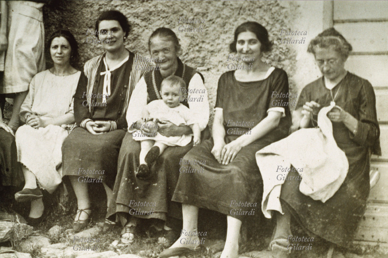 GOZZO Gruppo fotografico femminile di famiglia; la nonna con un bimbo in braccio è affetta da gozzo, un aumento di volume della ghiandola tiroide ad andamento benigno. La donna sulla destra non si fa ritrarre con le mani in mano, ma impegnata a cucire. Italia, inizio del XX secolo.