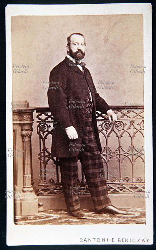 RITRATTO maschile a figura intera, eseguito in atelier, in piedi accanto ad una ringhiera in ferro battuto. L\