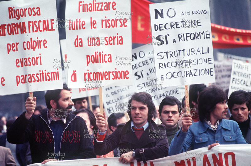 STORIA DEL MOVIMENTO OPERAIO Manifestazione commemorativa dei lavoratori per il Primo Maggio. Alcuni i cartelli di protesta: Rigorosa riforma fiscale per colpire evasori e parassitismi/ Finalizzare tutte le risorse da una seria politica di riconversione/ NO a un nuovo decretone SI a riforme strutturali riconversione e occupazione. Milano, Piazza del Duomo 1977