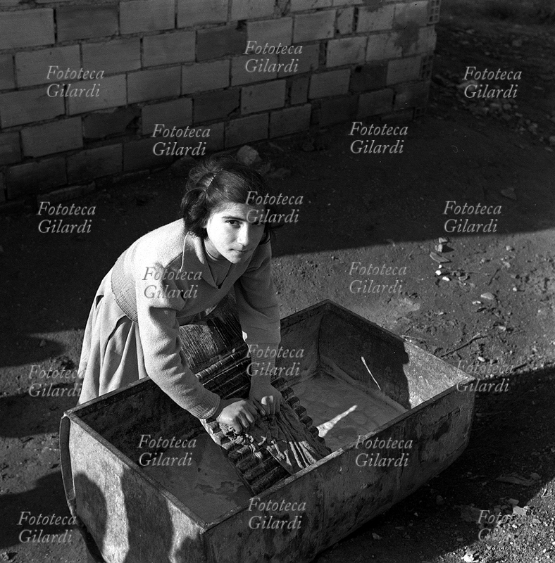 LAVANDAIA giovane donna lava i panni in un grande lavatoio rettangolare con un asse di legno a \