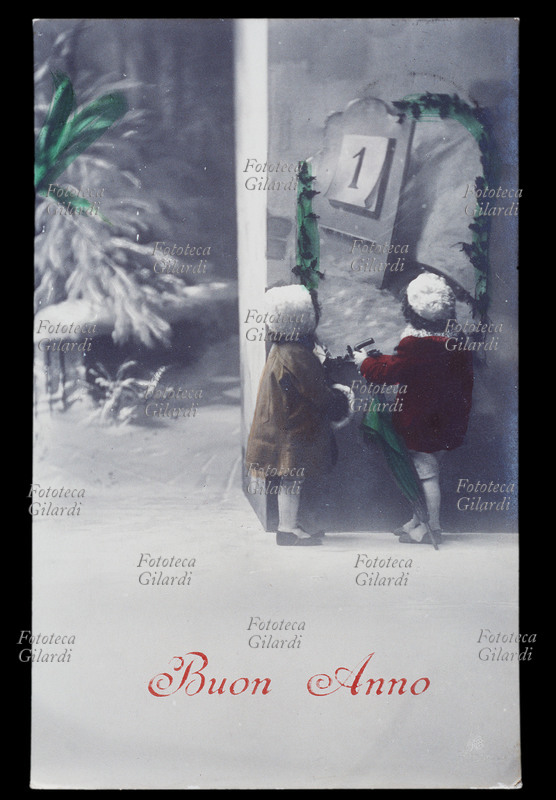 CAPODANNO due bambine vestite con pesanti cappotti, cappelli di pelliccia, galosce e ombrello, guardano sul calendario il primo giorno del nuovo anno e si preparano ad uscire: fuori nevica. Fotografia acquarellata, Italia 1915.