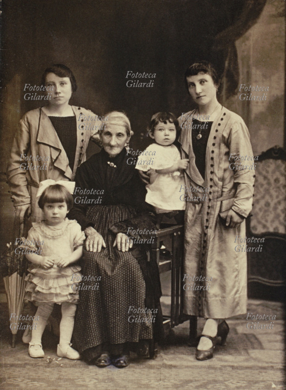 FAMIGLIA fotogruppo matriarcale, due sorelle gemelle molto somiglianti, anche perché vestite uguali, in posa con la madre anziana e due figlie bambine. Fotografia di anonimo, formato gabinetto. Italia, 1915 circa.