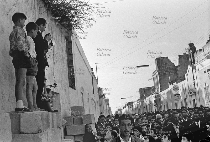 SAN DONACI Fotografo in piedi fra i bambini su una catasta di blocchi a bordo strada, riprende dall\