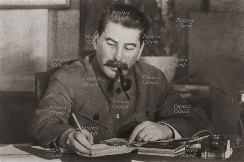 STALIN (1879-1953) Ritratto fotografico mentre lavora alla scrivania, fumando la pipa. URSS 1945